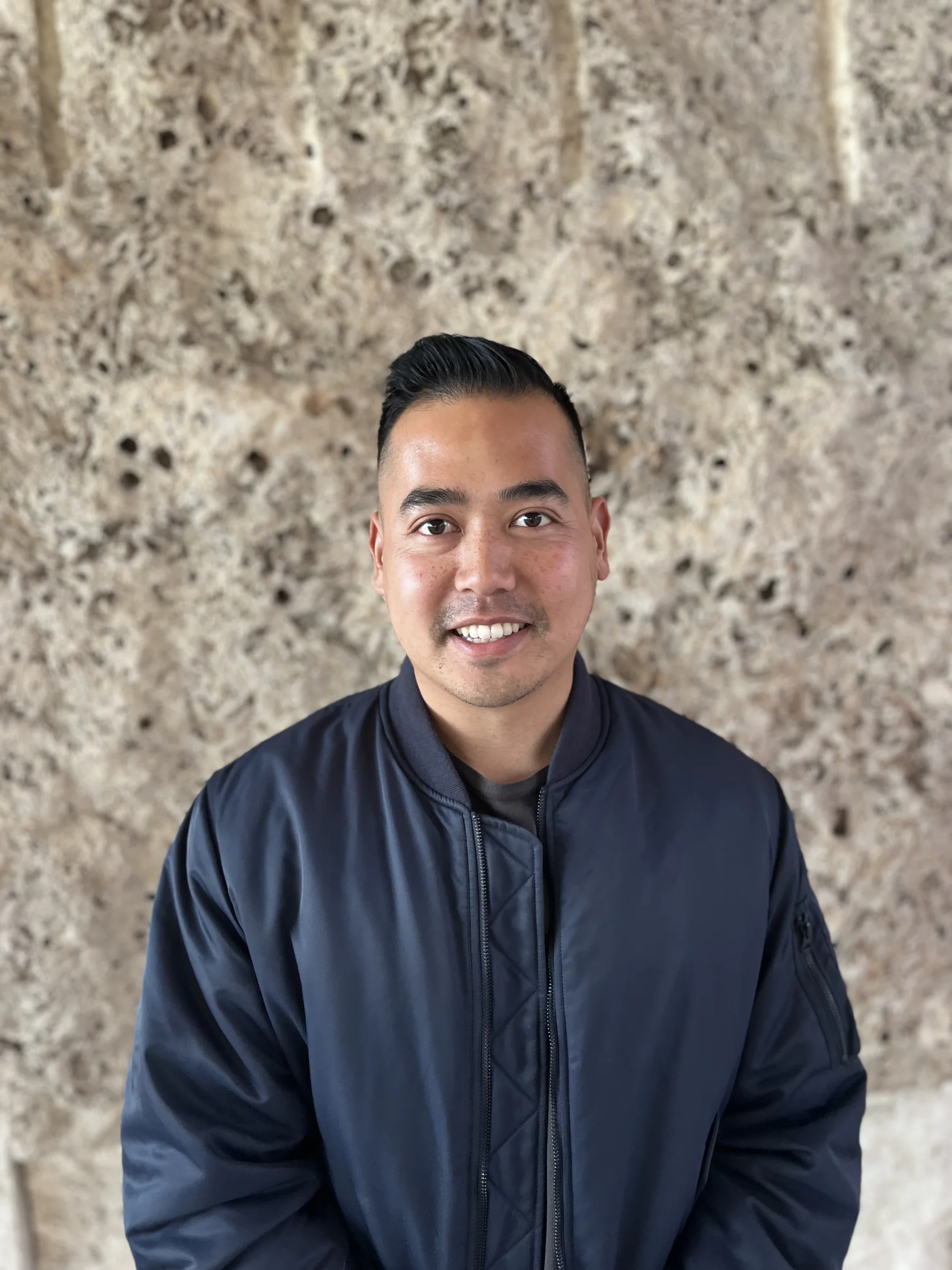 Stanley Yang smiling in front of a stone wall